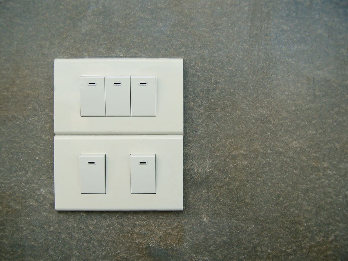 Duas placas brancas na parede de cimento, uma com três teclas e outra com duas teclas de interruptor